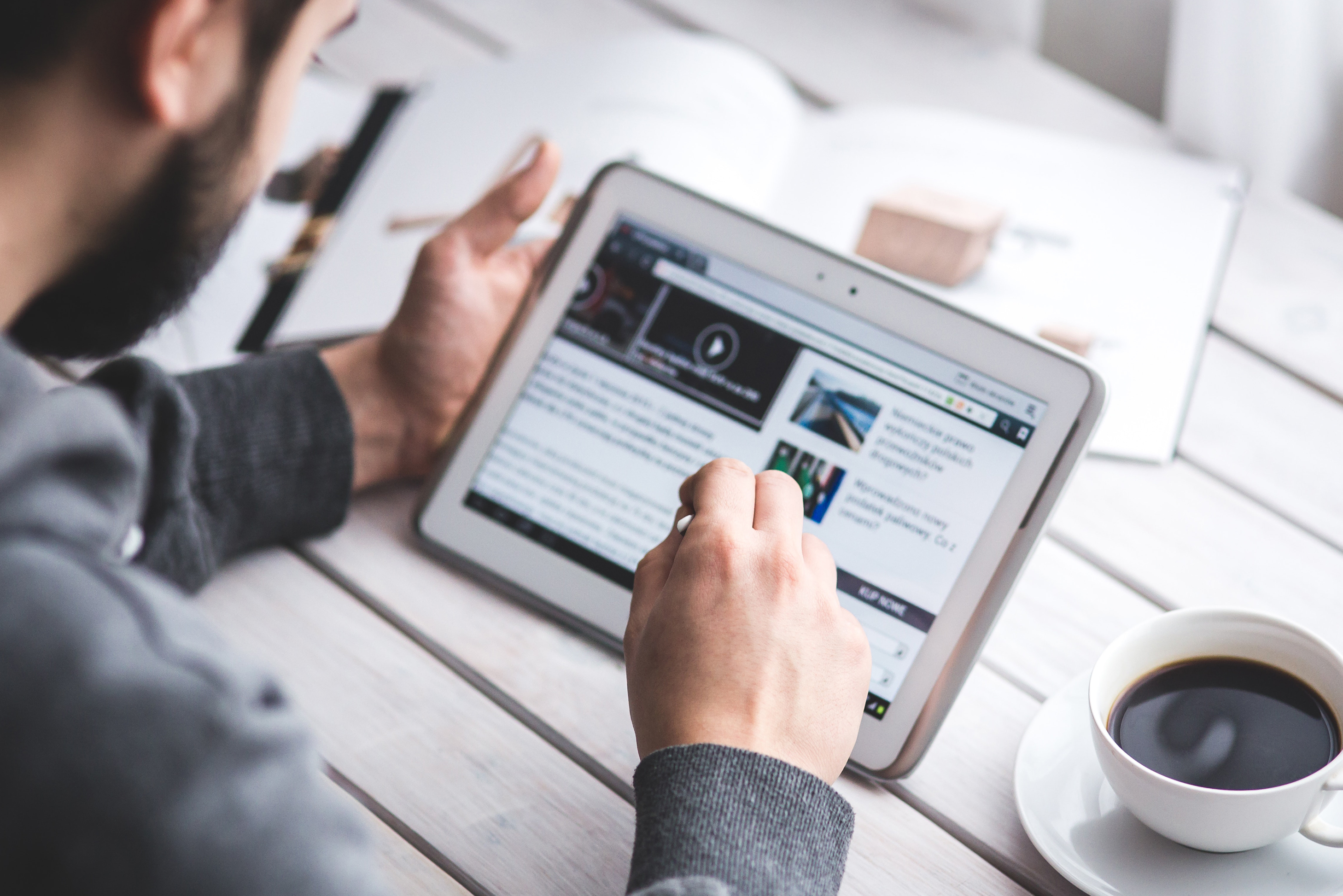 man using a tablet on a wooden table.