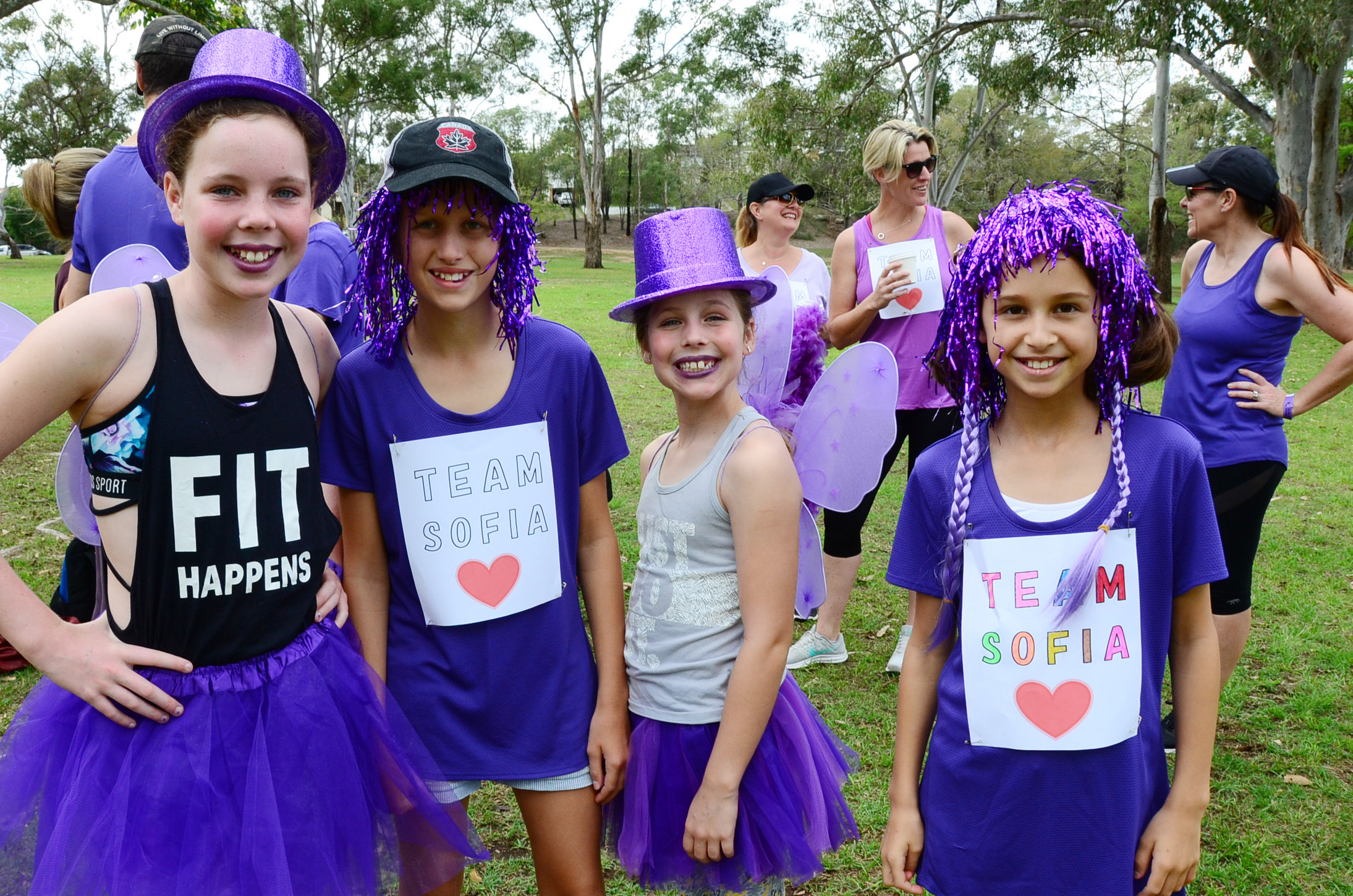 girls in purple tutus and hats smiling for a photo.