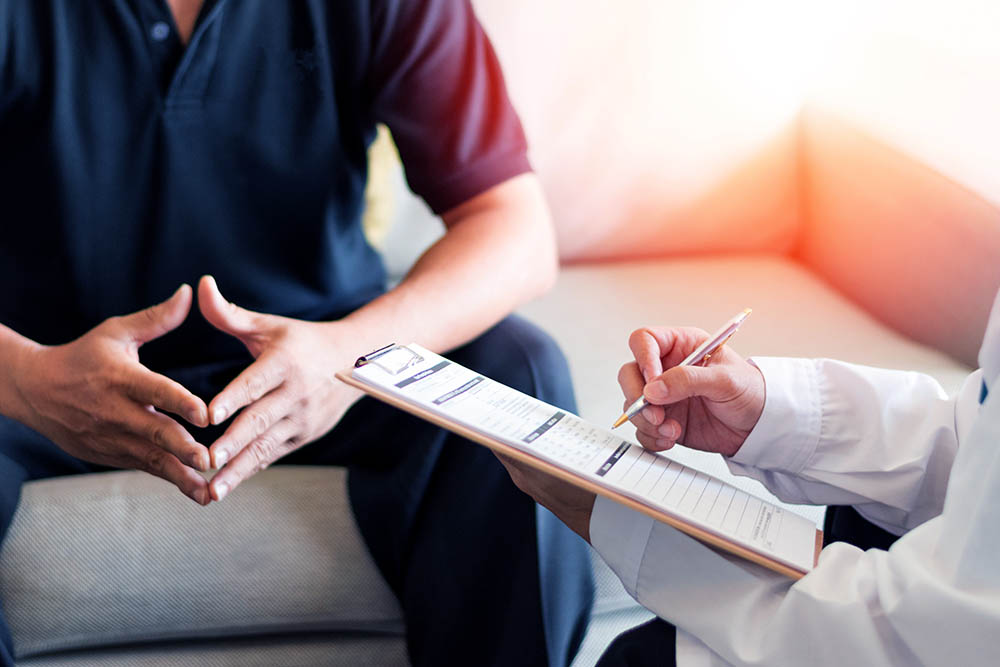 Man sits on couch with a medical professional holds a clipboard