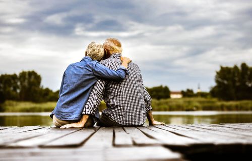 Two elderly individuals enjoying a serene moment on a dock, gazing at the calm waters ahead.