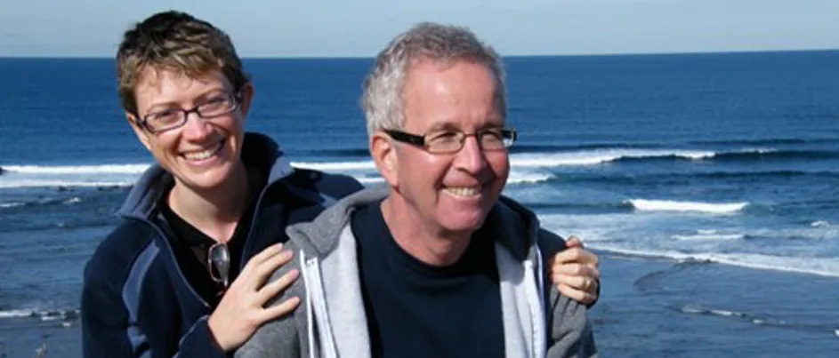 Caroline and Avner together by the ocean, smiling with their arms around each other.