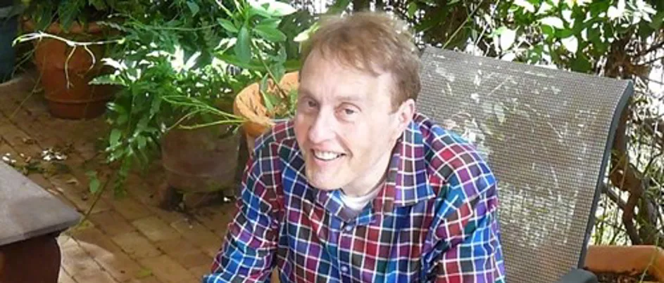 Tim, wearing a checkered shirt, sitting and smiling at the camera.