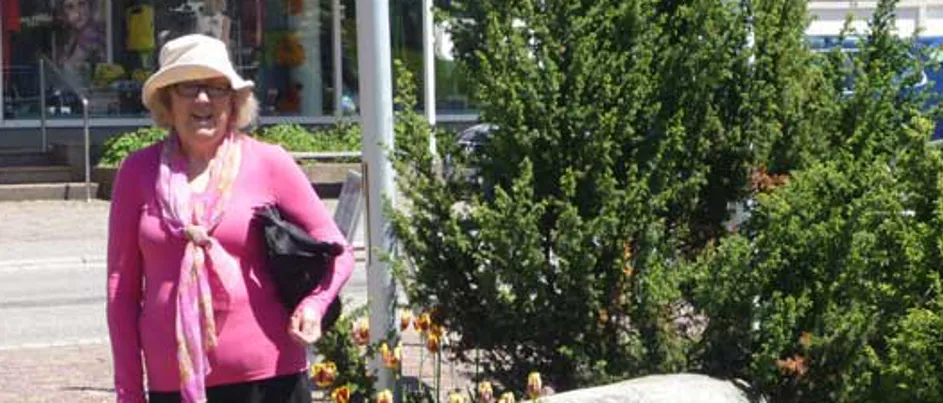 Judith, a woman wearing a pink top, standing next to a garden of flowers.