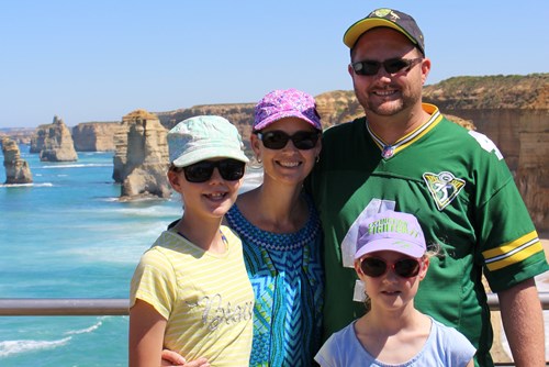 Ryan standing with his wife and two daughters with the iconic Australian coastline in the background. 
