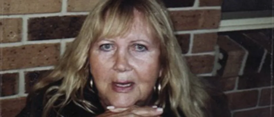 Rayna's mum looking into the camera with her hands interlocked in front of her.