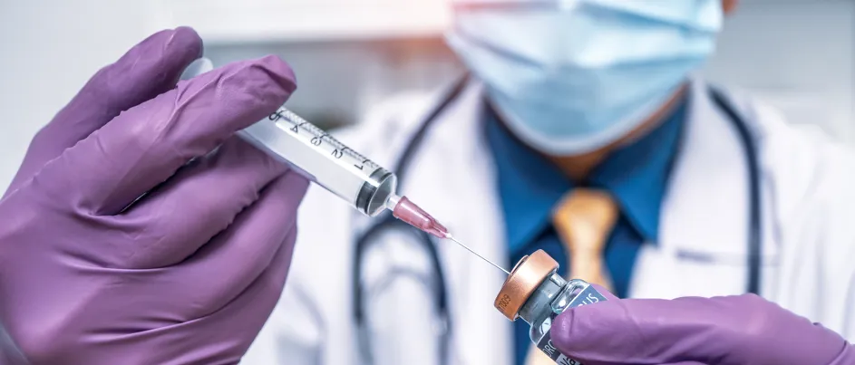 "A medical professional wearing a white coat, purple gloves, and a face mask fills a syringe preparing an injection, working on a cancer vaccine."